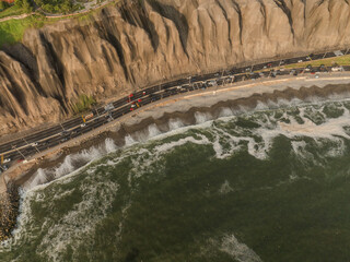 The green colored sea hits the rocks beside a highway and cliff in Miraflores, Lima, Peru.