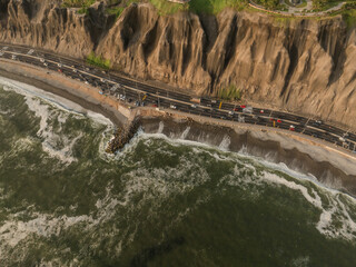 The green colored sea hits the rocks beside a highway and cliff in Miraflores, Lima, Peru.