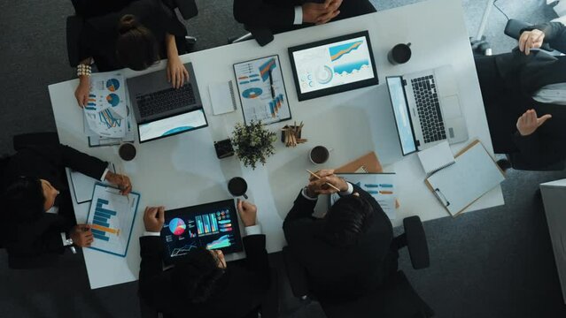 Top down aerial view of smart manager pointing at financial graph on whiteboard while diverse business team explain and plan marketing idea at meeting table with stock market statistic. Directorate.