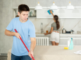 Guy mops floor until it shines during group cleaning in kitchen - obrazy, fototapety, plakaty