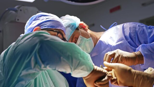 Hard-working male Caucasian surgeons co-working at trauma surgery. Doctors use metal instruments at operation.