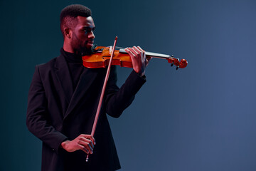 Talented young African American man playing violin in a captivating performance on a dark blue...