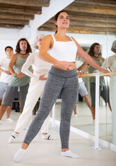 Young athletic woman performs exercises at barre in gym