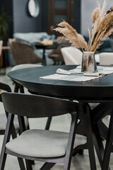 Black wooden table complete with black wooden chairs with soft gray fabric upholstery. Glass vase on the table