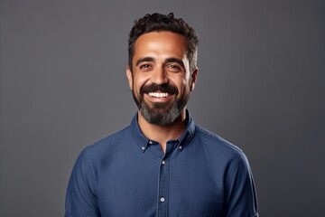 Portrait of a handsome bearded man smiling at the camera while standing against grey background - obrazy, fototapety, plakaty