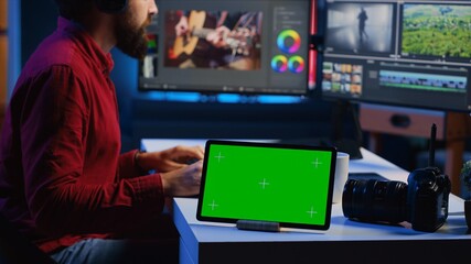 Green screen tablet on desk in multimedia agency next to video editor working for independent production company inputting music, dialogues, graphics and effects over raw footage