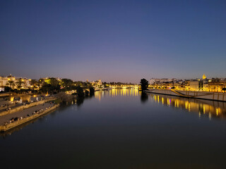 View of the Guadalquivir River in the night illuminations at sunset in Seville, Andalusia, Spain