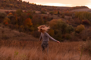 Young attractive blonde woman standing on the hill at sunset	