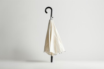 A classic, cream-colored closed umbrella with a stylish hook handle stands against a white background - obrazy, fototapety, plakaty
