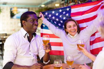 People different ages with USA flag are resting on the event in bar.