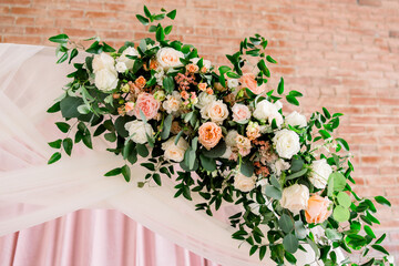 An elegant rose and floral centerpiece and greenery decorating a wedding arch inside a brick building.