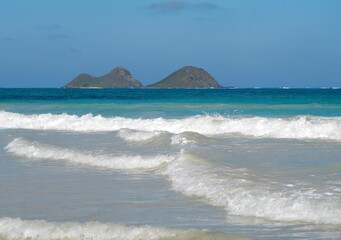 looking toward moku iki island across the azure waters and surf of the pacific ocean, from the bellows field beach park on the windward coast of oahu, hawaii