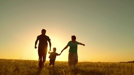 Happy family runs in park at sunset. Silhouette of happy family in park. Mom dad son family walk....