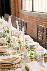 An elegant head table in a brick warehouse. The table is decorated with candlesticks, plates and menus, and greenery and florals.