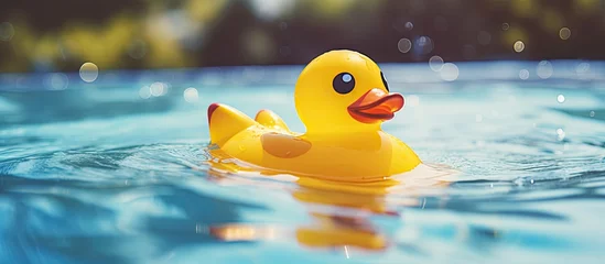Fotobehang A bath toy in the shape of a yellow rubber duck is peacefully floating in the crystalclear pool of water. Ducks, geese, and swans are all waterfowl, but this particular organism is a toy bird © TheWaterMeloonProjec