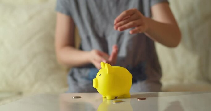 Child saving coins in a piggy bank dream close-up. Child hands puts coins in a large piggy bank indoors. Child hands hoarding coins put in piggy bank. Happy family accumulation business concept. 4K