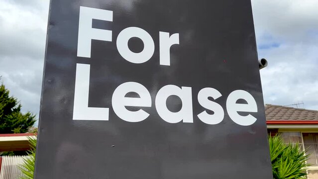 a bold 'For Lease' sign with a suburban house in the background, concept of a property ready for new tenants or occupants in a residential area, housing market, and rental vacancy.