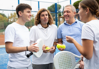 Two pairs with rackets in their hands chatting after playing padel on the tennis court - obrazy, fototapety, plakaty