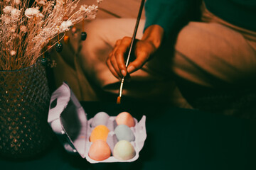 Colorful painted Easter eggs in a violet box, a paint brush in woman's hands. Vibrant colors....