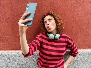 Redhead woman taking a playful selfie against a red wall