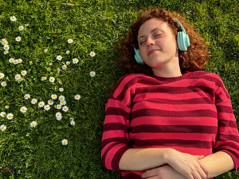 Young redhead woman relaxing on grass with headphones