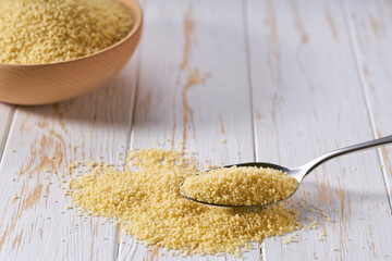 metal spoon with organic couscous on a white wooden table.