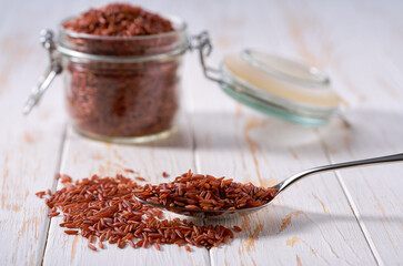 metal spoon with raw red rice on a light table, selective focus.