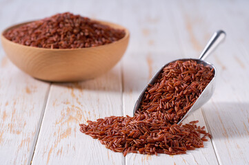 Raw red rice in a metal scoop on a white wooden table.