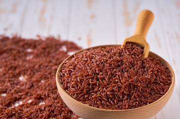 Raw red rice are scattered in a wooden bowl close up.