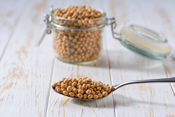 metal spoon with raw soybeans on a light table, selective focus.
