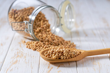 soybeans in wooden scoop and in glass storage jar on a white wooden table.