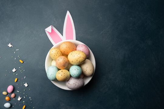 easter eggs with bunny ears and candy on a dark textured surface