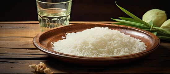 A dish of jasmine rice, a staple food ingredient in cuisine, rests on a wooden table alongside a...