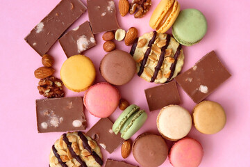 Pastel macarons, almond chocolate, peanut butter cookies and various nuts on bright pink background. Top view.