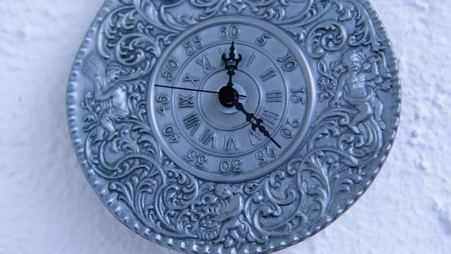 vintage silver clock of 19th century on white wall counts down the time, the hands move on dial, concept of road of life, time goes by, an irreversible flow from past, through present to future