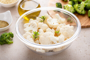 Raw cauliflower florets in a glass bowl, ready to roast with spices and olive oil