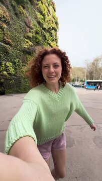 Young redhead woman taking a selfie while skating in front of a living wall