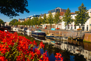 Mark River embankment in Breda, Netherlands. View of red flowers in bloom, buildings and boats...