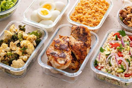 Healthy meal prep with cooked chicken breast, boiled eggs, roasted vegetables, cooked lentils, couscous salad and nuts