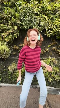 Young redhead woman dancing with phone and celebrating life outdoors