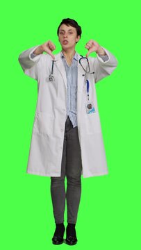 Front view Displeased physician showing thumbs down symbol against greenscreen backdrop, expresses negativity and rejection. Doctor feeling dissatisfied and disagreeing with an idea, dislike sign