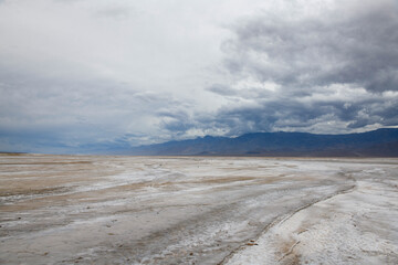 Salt flats at badwater basin in Death Valley with distant mountains under a gloomy sky