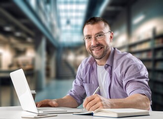 Smart male student at desk using laptop,