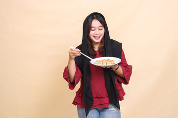 Beautiful mature Asian woman wearing a red hijab happily picks up chopsticks and carries a plate containing dimsum (Chinese food) see below. used for food, health and lifestyle content