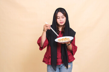 beautiful mature Asian woman wearing a red hijab, pouting cutely, taking chopsticks and carrying a plate containing dimsum (Chinese food) see below. used for food, health and lifestyle content