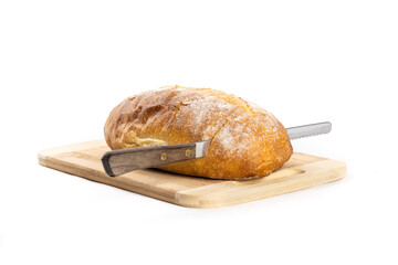 A single loaf of Italian or French crusty bread on a wooden board with a serrated bread knife...