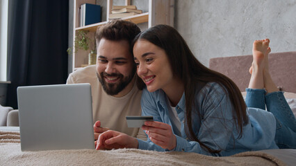 Caucasian couple happy woman and man looking at laptop screen on home bed excited smiling wife and husband pay money online use bank credit card family budget e-commerce buy goods shopping for bedroom - Powered by Adobe