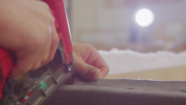 Close-up of a worker's hands stapling upholstery on a boxspring bed in a bright factory