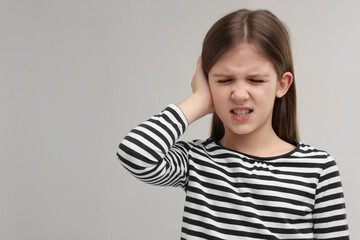 Hearing problem. Little girl suffering from ear pain on grey background, space for text