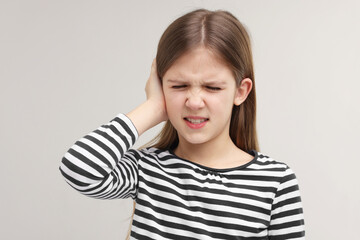 Hearing problem. Little girl suffering from ear pain on grey background